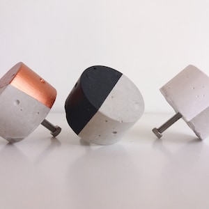 May include: Three concrete cabinet knobs with different finishes. One is painted black and white, one is painted copper and white, and one is all white.