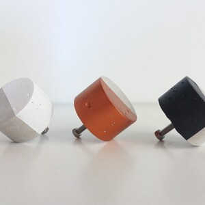 May include: Three concrete cabinet knobs with a white and coloured design. The knobs are in shades of grey, copper, and black.