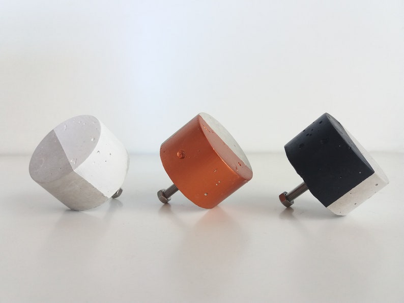 May include: Three concrete cabinet knobs with a white and coloured design. The knobs are in shades of grey, copper, and black.