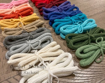 May include: A collection of crocheted cords in various colors, including pink, red, maroon, blue, teal, green, gray, and white. The cords are arranged in a row on a wooden surface. The text "Crochet 'N Things by Rachael" is visible in the lower left corner of the image.