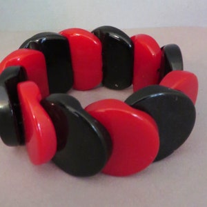 Peut inclure: Un bracelet en plastique rouge et noir avec des perles rondes et plates. Les perles sont disposées en un motif répétitif de rouge et de noir.