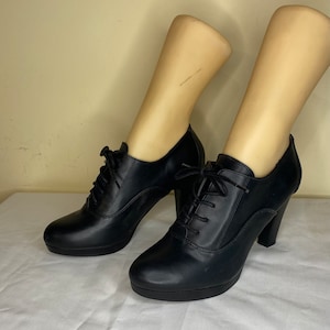 Op de afbeelding: Zwarte leren enkellaarsjes met veters en een dikke hak.