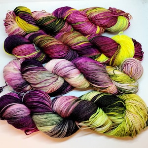 May include: Four skeins of yarn in a multi-colored pattern of pink, purple, green, and yellow. The yarn is arranged in a criss-cross pattern.