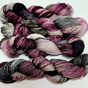 May include: A skein of yarn in shades of burgundy, gray, and cream. The yarn is hand-dyed and has a variegated color pattern.