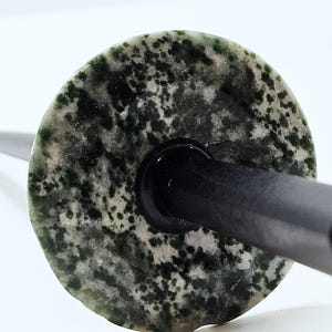 May include: A close-up of a bottle stopper with a circular, speckled green and white stone top. The stopper has a black base and a dark gray stem. The stone has a natural, organic pattern.