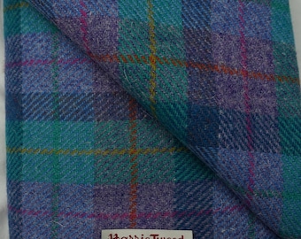 May include: A close-up of a folded piece of Harris Tweed fabric in a blue, green, and purple plaid pattern. The fabric has a label that reads "Harris Tweed, Hand Woven in the Outer Hebrides".
