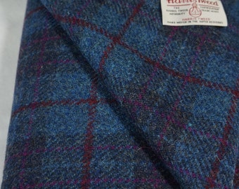 May include: A close-up of a blue and burgundy plaid fabric with the Harris Tweed label. The label reads "The Harris Tweed Authority" and "Hand Woven in the Outer Hebrides".