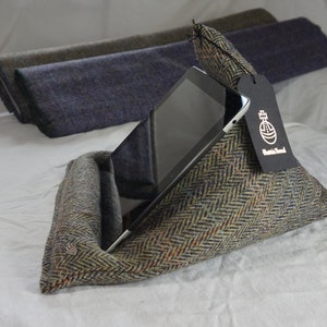 May include: A green, brown, and blue tweed tablet stand with a black tag that says "Handmade Tweed". A black tablet is propped up in the stand.