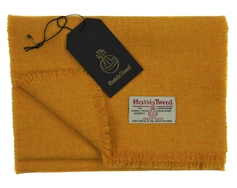 May include: A yellow Harris Tweed scarf with a fringed edge. The scarf has a label that reads "Harris Tweed" and includes the Harris Tweed Orb logo.