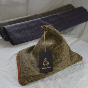 May include: A brown and blue tweed fabric sample with a brown tag that says "Harris Tweed" in gold lettering. The fabric is folded into a triangular shape.
