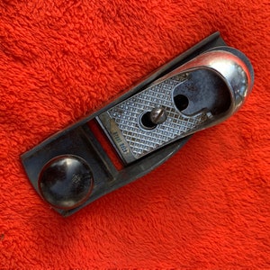 May include: A vintage wooden hand plane with a metal blade and a black handle. The plane is labeled "Stanley No. 93".