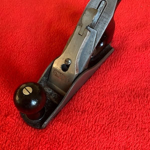 May include: A vintage Stanley hand plane, featuring a metal blade and body with a black wooden knob and handle. The tool is marked "STANLEY" and "MADE IN U.S.A.", showcasing its craftsmanship. The plane is designed for woodworking and carpentry.
