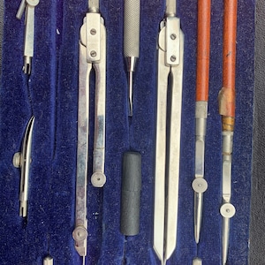 Puede incluir: Un conjunto de herramientas de dibujo vintage en un estuche de terciopelo azul. Las herramientas incluyen compases, un transportador, una regla y un lápiz. Las herramientas están hechas de metal y tienen un acabado plateado.