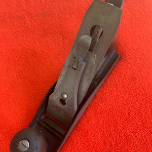 May include: A black wooden hand plane with a metal blade and a black knob. The plane is labeled "GUNLAP" and has a serial number "39166".