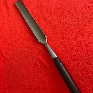 May include: A woodworking gouge with a curved, beveled blade and a dark wooden handle. The metal blade is silver and the handle is a dark brown color. The tool is designed for shaping and carving wood.