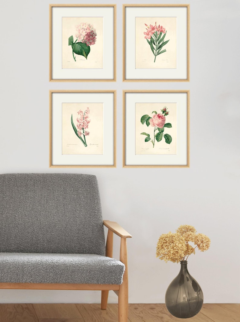 May include: Set of four framed botanical prints featuring pink flowers. The prints are in a simple white frame with a light wood border. The prints are arranged in a grid pattern on a white wall.