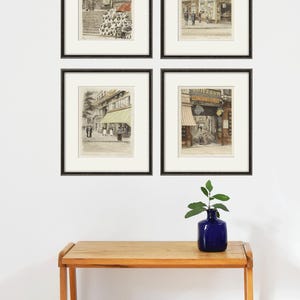 Puede incluir: Cuatro impresiones vintage de escenas de calles parisinas enmarcadas en negro. Las impresiones est&aacute;n dispuestas en una cuadr&iacute;cula en una pared blanca. Una peque&ntilde;a planta en maceta se encuentra sobre una mesa de madera debajo de las impresiones.
