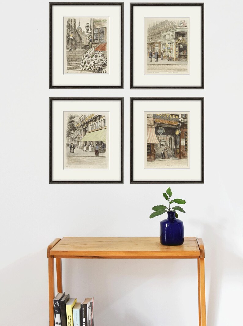 Puede incluir: Cuatro impresiones vintage de escenas de calles parisinas enmarcadas en negro. Las impresiones est&aacute;n dispuestas en una cuadr&iacute;cula en una pared blanca. Una peque&ntilde;a planta en maceta se encuentra sobre una mesa de madera debajo de las impresiones.