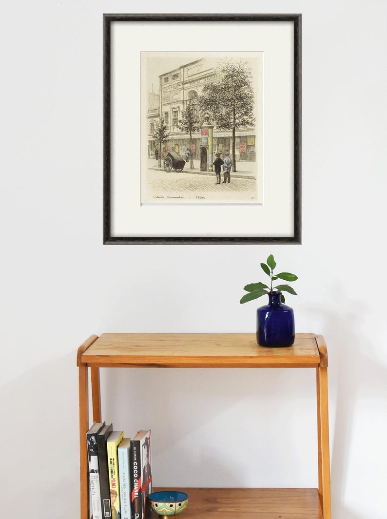 Puede incluir: Una impresi&oacute;n enmarcada en blanco y negro de una ilustraci&oacute;n vintage de un edificio con dos personas de pie frente a &eacute;l. El edificio tiene un letrero que dice "Caf&eacute;" y la impresi&oacute;n se titula "Caf&eacute; Commerzienrath".