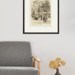 Puede incluir: Un dibujo en blanco y negro de una escena callejera en una ciudad europea. El dibujo muestra un edificio con un gran escaparate y varias personas caminando. El dibujo est&aacute; enmarcado en un marco negro.
