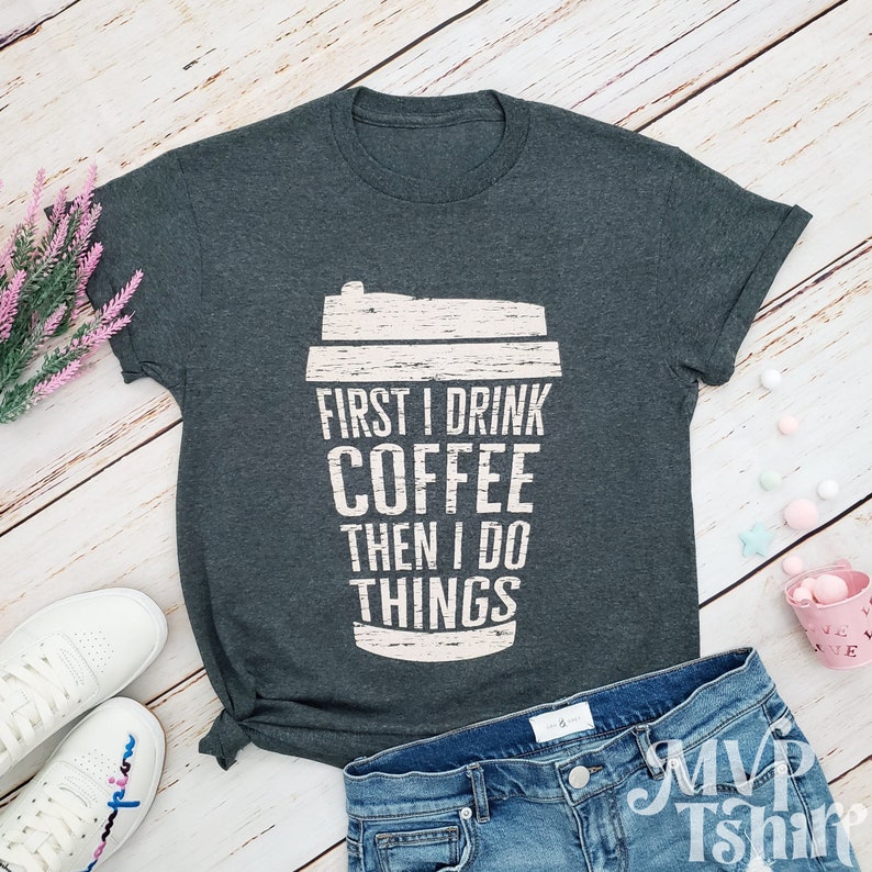 May include: A dark gray t-shirt with a distressed white graphic of a coffee cup and the text "First I drink coffee then I do things".