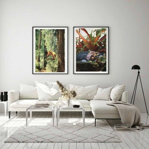 May include: Two framed art prints. The left print depicts a person in a forest, the right print shows a person among plants. The prints are displayed above a white sofa with white tables and a patterned rug. A black floor lamp is in the background.