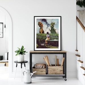 May include: A framed print of a woman sitting at a table in a garden with two dinosaurs looking over the fence. The dinosaurs are green and brown and the woman is wearing a white dress. The print is on a white wall with a plant in a pot on a table in front of it.