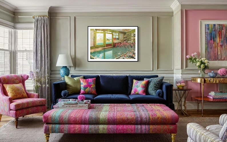 May include: A living room interior with a blue velvet sofa, a colorful patterned ottoman, and a framed print of a swimming pool scene. The room is decorated with colorful throw pillows and a lamp with a blue base.