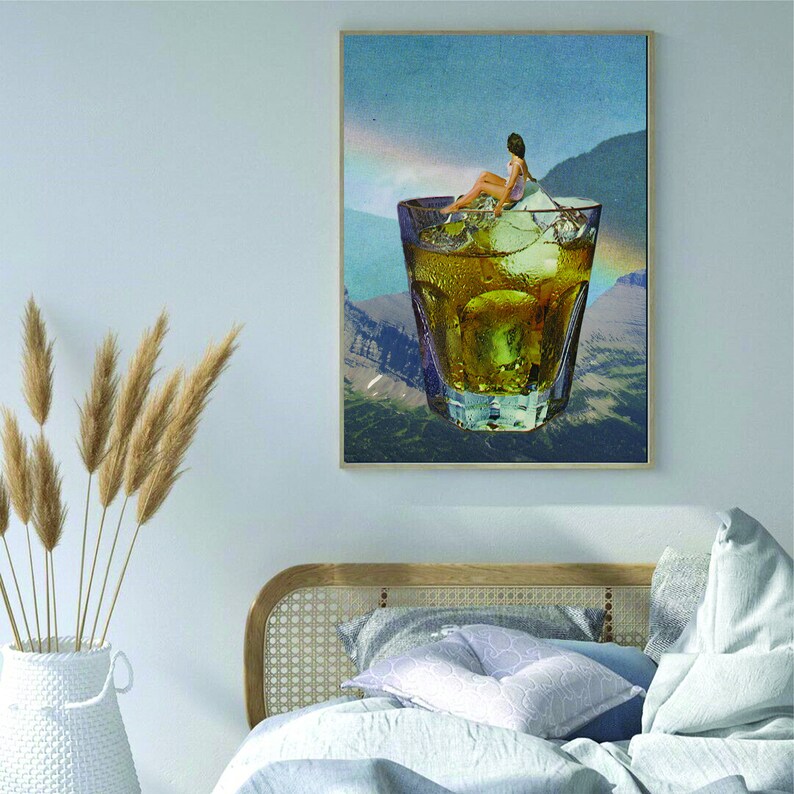 May include: A collage art print featuring a woman sitting on a large ice cube in a glass of amber liquid. The glass is surrounded by a mountain landscape with a blue sky and clouds.