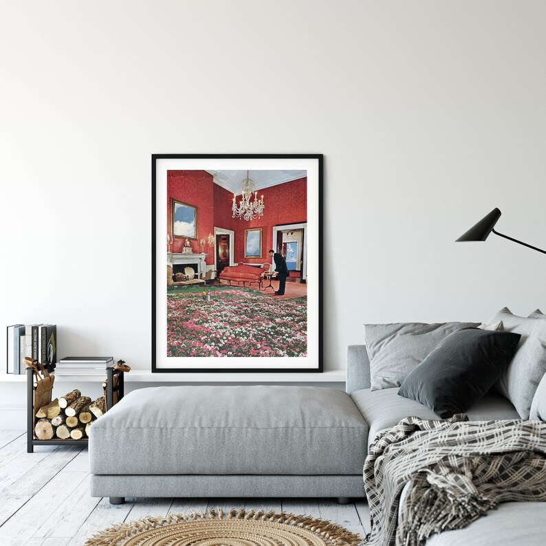 May include: A framed print of a surrealist photograph depicting a red room with a floral carpet, a chandelier, and two figures standing in the room.