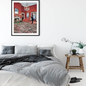 May include: A framed print of a surrealist photograph depicting a man standing in a room with a red wall and a green and white floral carpet.