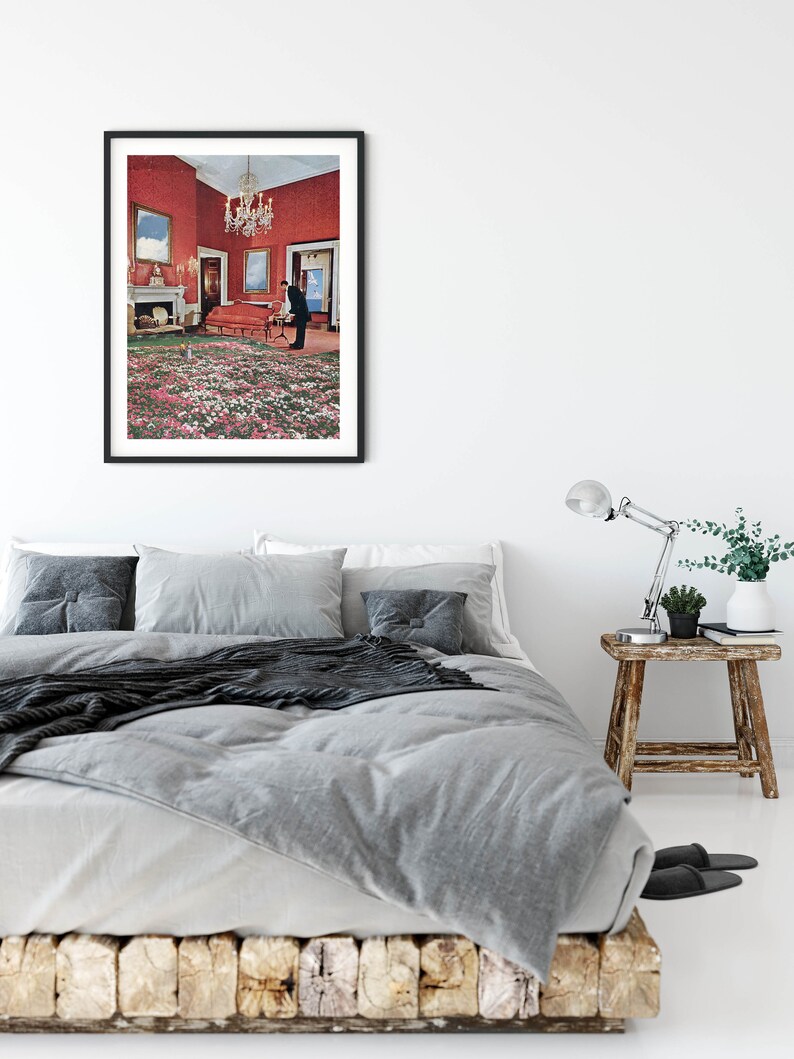 May include: A framed print of a surrealist photograph depicting a man standing in a room with a red wall and a green and white floral carpet.
