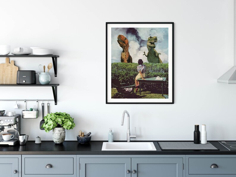 May include: A framed collage print featuring a woman sitting at a table in a garden setting with two dinosaurs in the background. The dinosaurs are green and brown and appear to be looking at the woman. The print has a vintage aesthetic.