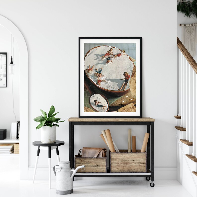 May include: A framed collage of a vintage photograph of children playing in a large bowl of whipped cream. The image is in a black frame and is hanging on a white wall.