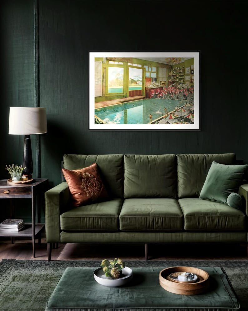 May include: A framed print of a vintage illustration depicting a swimming pool inside a building with a view of a lake and mountains through the windows. The pool is surrounded by people in bathing suits and there are umbrellas and chairs around the pool.