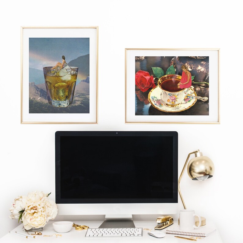 May include: A computer monitor with a black screen sits on a desk with a gold lamp, a white mug, a keyboard, and a gold stapler. Two framed pictures hang on the wall behind the desk. One picture shows a glass of whiskey with ice and the other shows a cup of tea with a red rose.