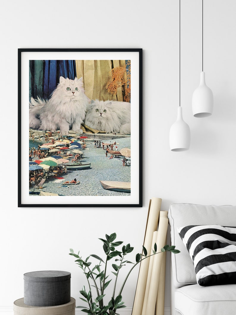May include: Two white Persian cats sitting on a beach scene with people and umbrellas. The cats are looking at the camera.