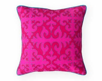 Pode incluir: Uma almofada rosa com uma borda azul e um padrão floral decorativo.