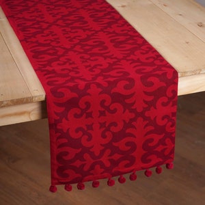 May include: Red table runner with a damask pattern and pom-pom trim.