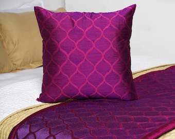 Può includere: Un cuscino decorativo di colore viola e rosa con un motivo geometrico. Il cuscino è su un letto con un copriletto a motivo viola e rosa.
