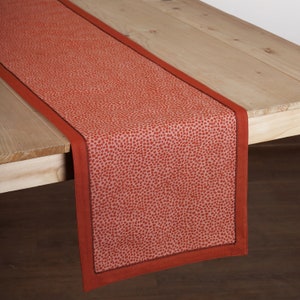 May include: A red table runner with a white background and a small, speckled pattern. The runner has a dark red border.