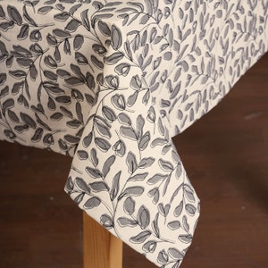 May include: A white tablecloth with a gray leaf pattern. The tablecloth is draped over a wooden table.