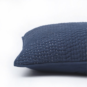 Op de afbeelding: Een donkerblauw gestikt kussen met witte stiksels. Het kussen is gemaakt van een zachte, comfortabele stof en heeft een eenvoudig, elegant ontwerp.