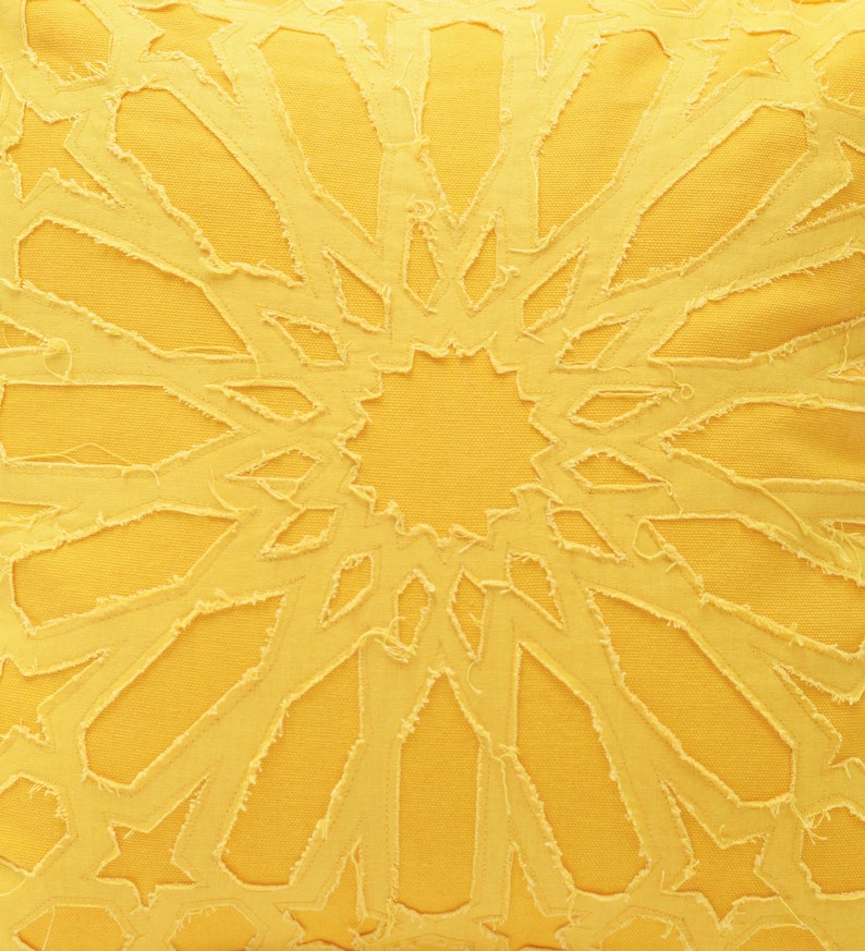 Pu&ograve; includere: Una federa quadrata giallo brillante con un motivo centrale a stella creato con ritagli di tessuto sfilacciati dai bordi grezzi. Il design &egrave; composto da forme geometriche che si irradiano dal centro, mostrando un aspetto stratificato e testurizzato.