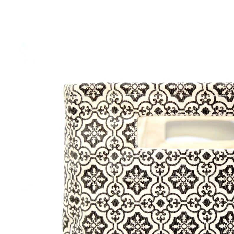 May include: A white fabric storage bin with a black and white geometric pattern. The bin has a cut-out handle on the side.