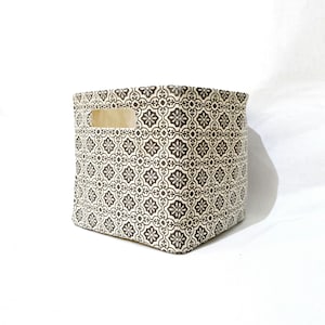 May include: A square, beige fabric storage bin with a black and white geometric pattern. The bin has a cut-out handle on the side.