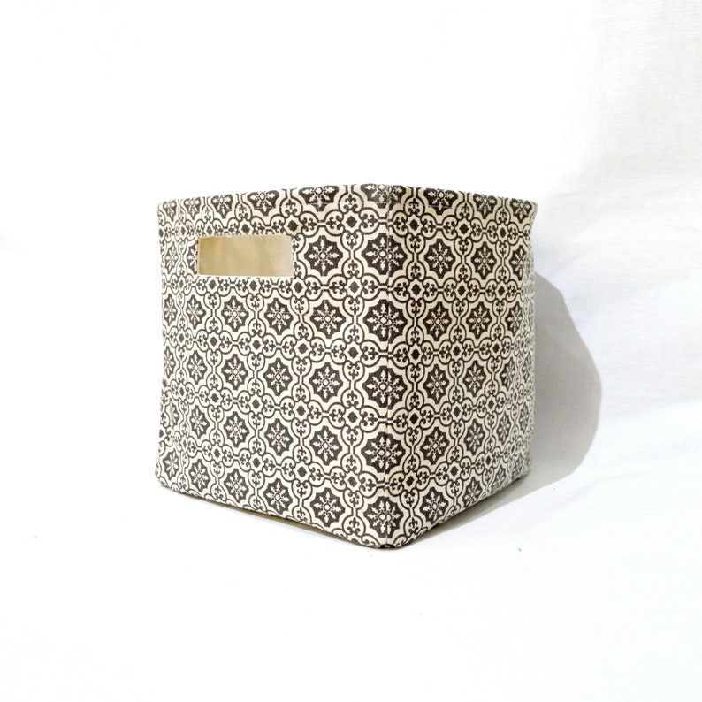 May include: A square, beige fabric storage bin with a black and white geometric pattern. The bin has a cut-out handle on the side.