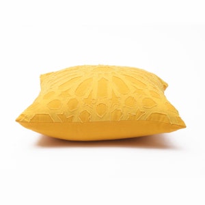 Pu&ograve; includere: Un cuscino quadrato color giallo senape con un motivo geometrico in rilievo sulla parte anteriore. Il design &egrave; composto da complesse forme a stella e poligoni intrecciati con bordi sfilacciati, che creano un aspetto stratificato e dimensionale.