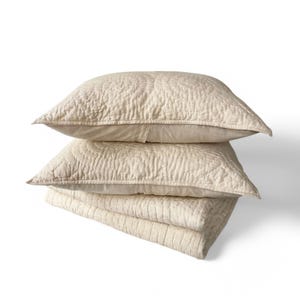 May include: A set of three cream-colored quilted pillowcases with a subtle textured pattern. The pillowcases are stacked on top of each other.