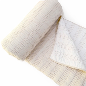 May include: A white cotton quilt with a subtle pink stitching pattern. The quilt is rolled up and partially unfurled, showcasing the intricate stitching detail.